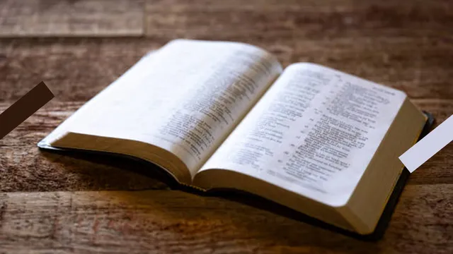 Je ziet een opengeslagen Bijbel liggen op een houten tafel.