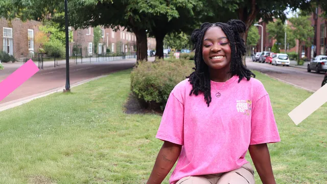 Je ziet hier Irene lachend in een stadspark. Ze draagt een roze t-shirt met de tekst 'Good news, Jesus loves you'. Op haar arm zie je haar littekens en de bijbeltekst Haggai 2:9.
