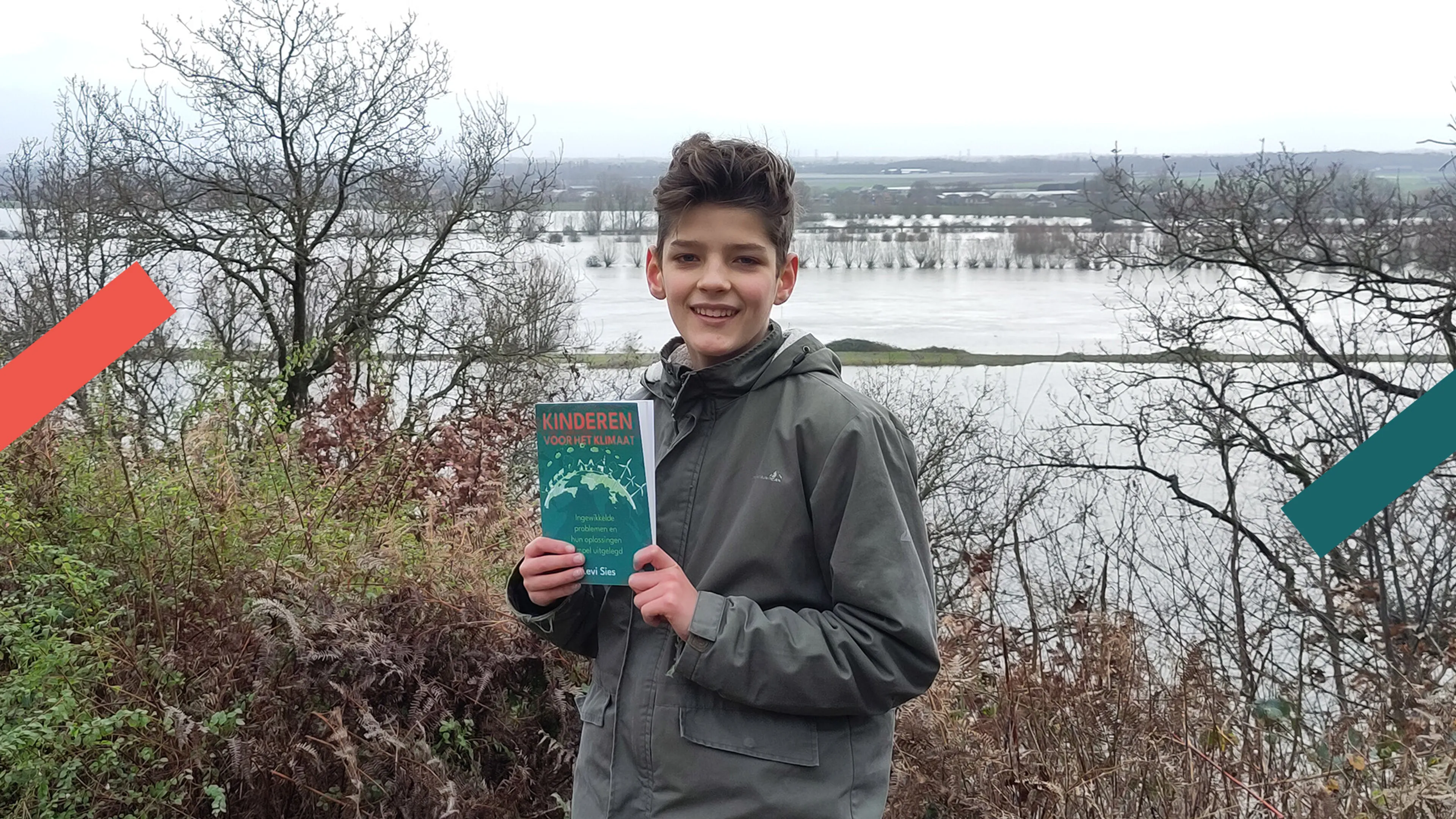 In het midden van de foto staat een jonge jongen met een groene jas aan. In zijn handen houdt hij een boek vast met een groene voorkant en de titel in rode letters. Op de achtergrond is een rivier te zien en kale bosjes.