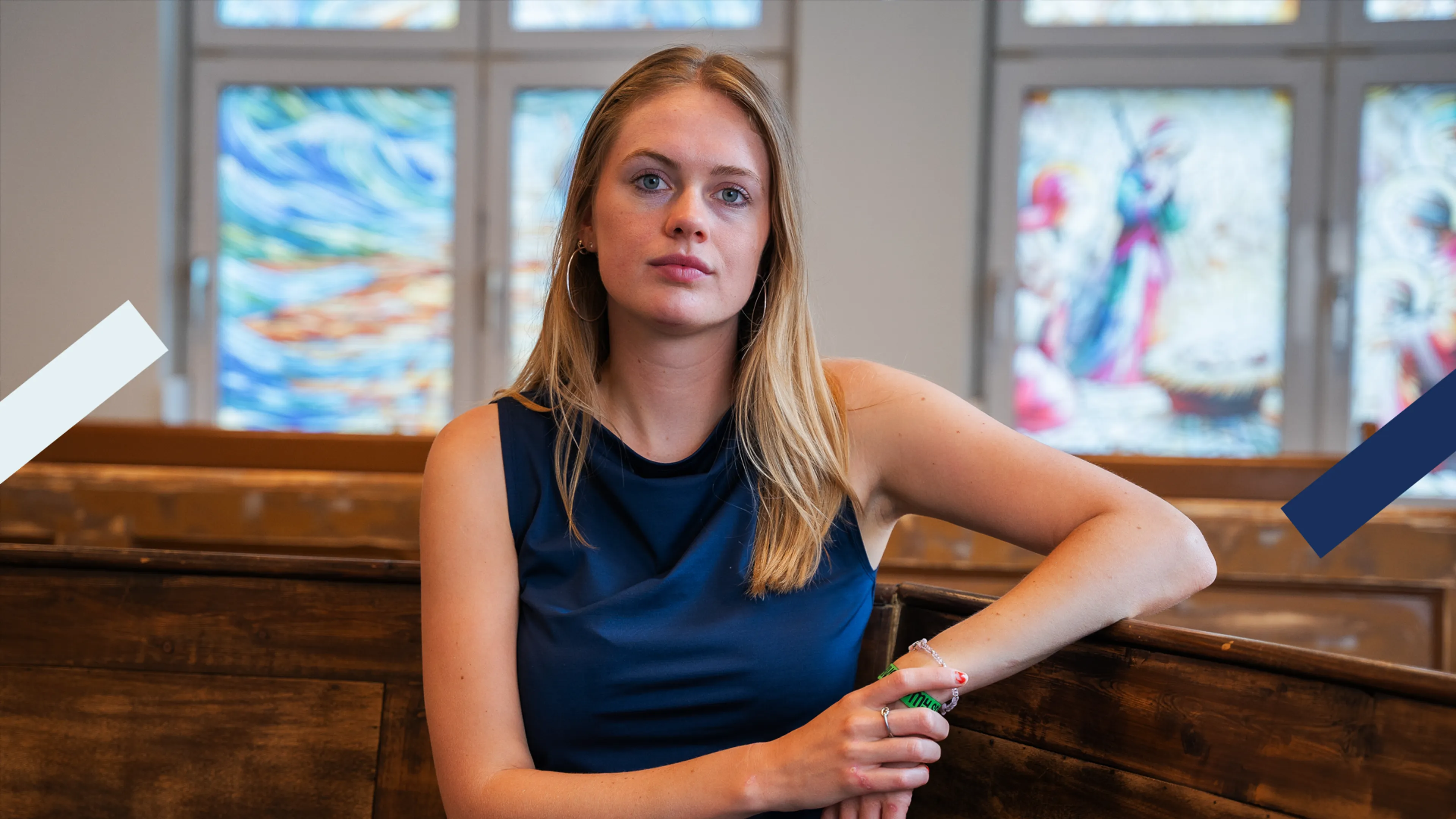 Jonge vrouw die zit op een kerkbank en serieus de camera inkijkt.