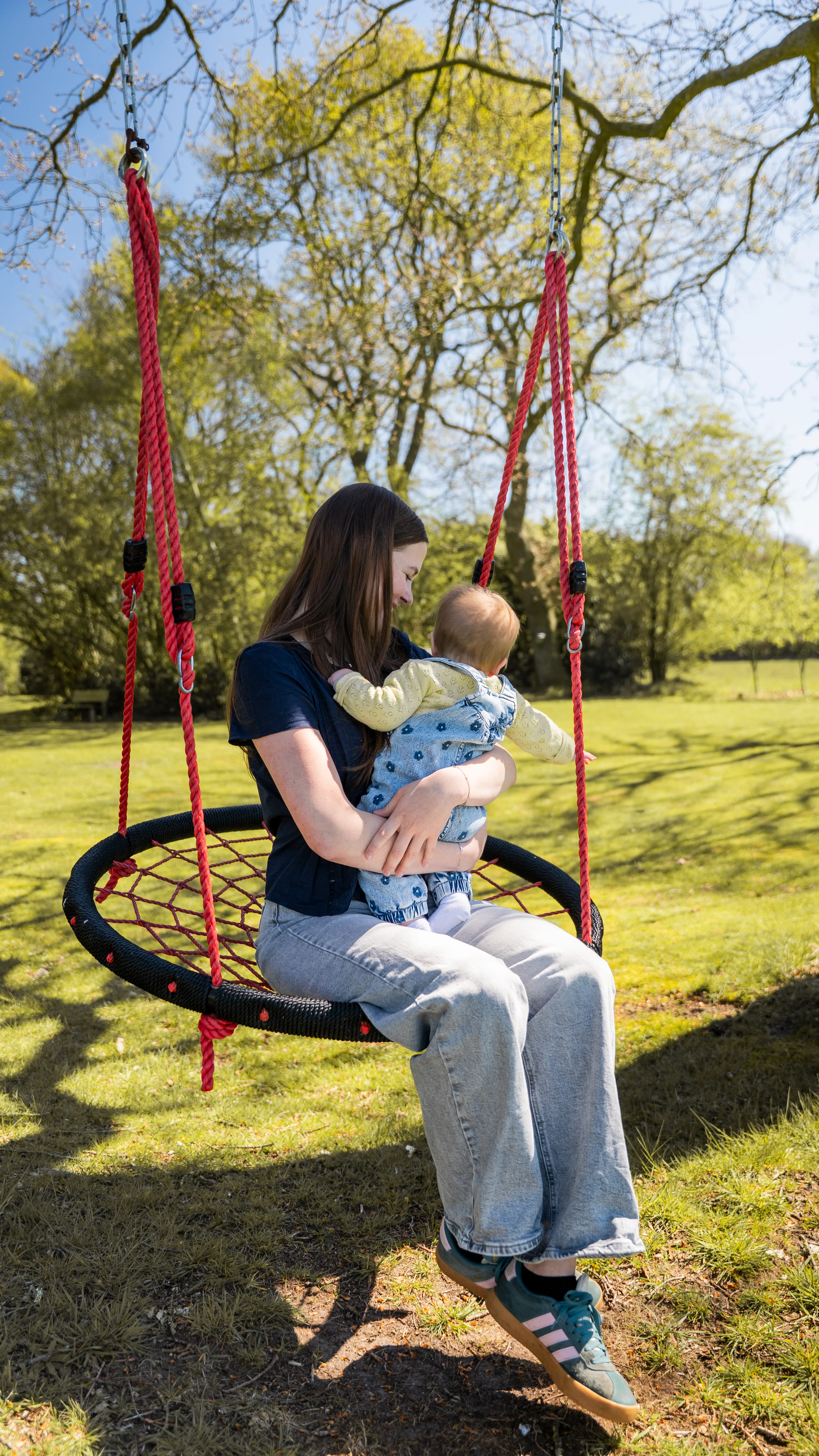 Charissa die in een schommel zit samen met haar baby. Ze kijk lief naar haar baby die de andere kant op kijkt.