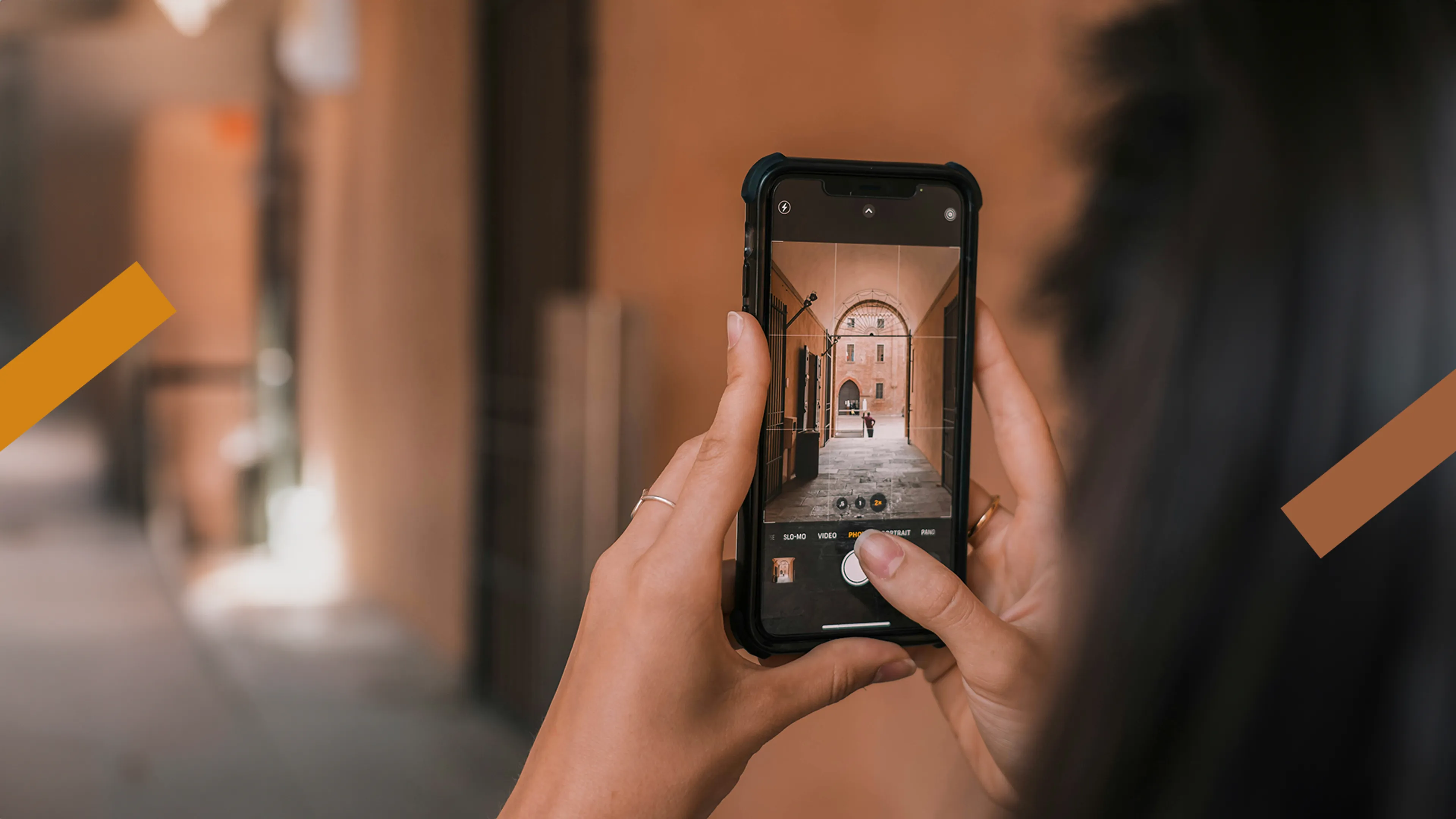 Je ziet twee handen die een smartphone vasthebben. Er wordt een foto gemaakt van een dorpje en je kan meekijken op het scherm.