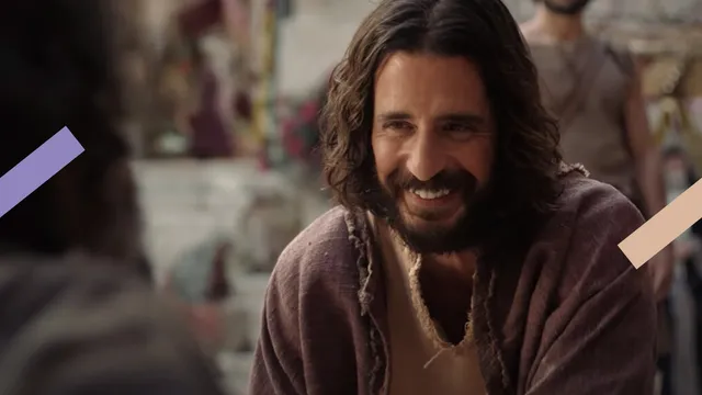 Je ziet de acteur Jonathan Roumie die de rol van Jezus speelt in The Chosen vriendelijk lachend naar iemand kijken.