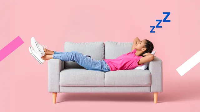 Een meisje met een roze t-shirt, spijkerbroek en witte allstars ligt te slapen op een kleine, grijze bank.