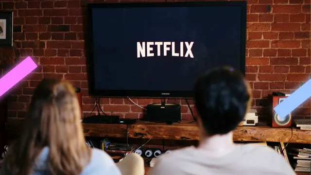 Een foto waarbij een jongen en een meisje op de bank zitten terwijl ze kijken naar een groot televisiescherm. Op dit scherm zie je het logo van Netflix.