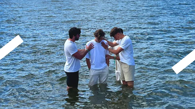 Je ziet Marc Floor in het wit gekleed tot zijn knieën in het water staan. Er staan jongens om hem heen die hem de handen opleggen. Het is het moment voordat hij onder water gaat en wordt gedoopt.