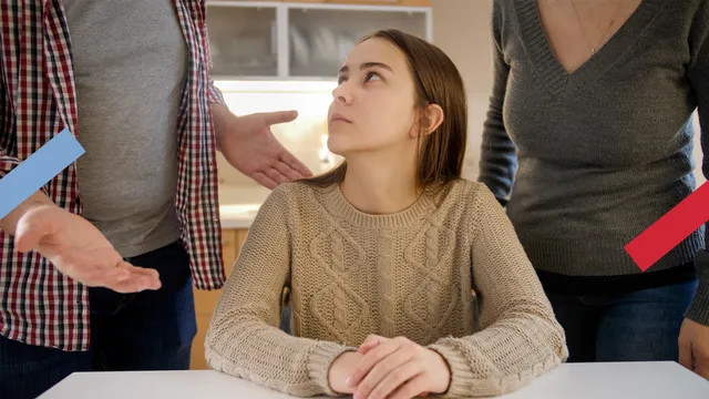 Je ziet een tienermeisje aan de keukentafel dat boos naar haar ouders kijkt die achter haar staan.