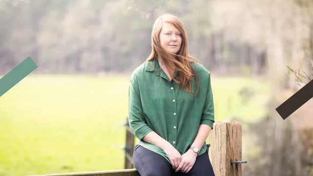 Redacteur Wilke zit buiten op een hek en staart met een neutrale blik voor zich uit. Ze draagt een groene blouse.