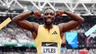Sprinter Noah Lyles laat zijn spierballen zien en lacht in de camera. Hij draagt een geel pak.