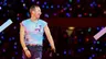 Chris Martin, de leadsinger van Coldplay, loopt over het podium. Achter hem zijn honderden blauwe lampjes te zien van mensen in het stadion.